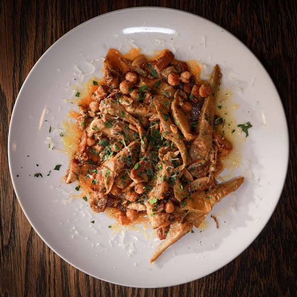 Pasta dish with chickpeas, shredded meat, and parsley on a white plate.