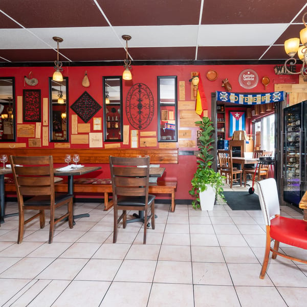Rustic restaurant dining room with red walls, wooden tables, Spanish decorations, chandeliers, and a glass-front wine refrigerator.