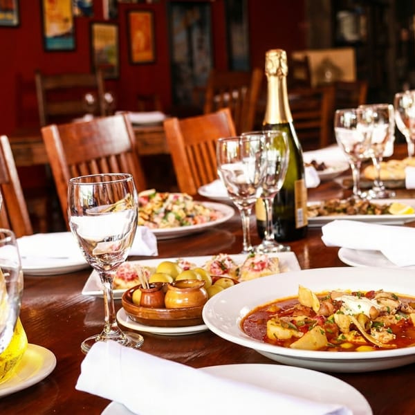 A long wooden table set with multiple dishes, wine glasses, and a champagne bottle in a restaurant.