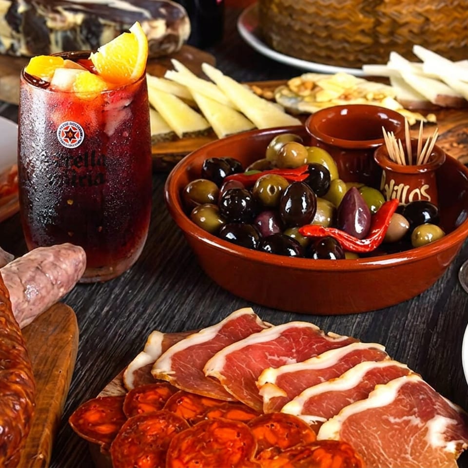 A Spanish tapas spread with cured meats, cheeses, olives, bread, and a glass of sangria.