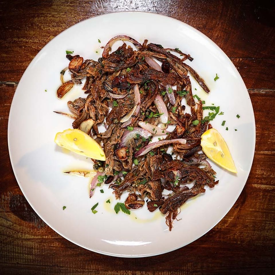 A white plate holds a dish of sautéed mushrooms and red onions, garnished with parsley and lemon wedges.