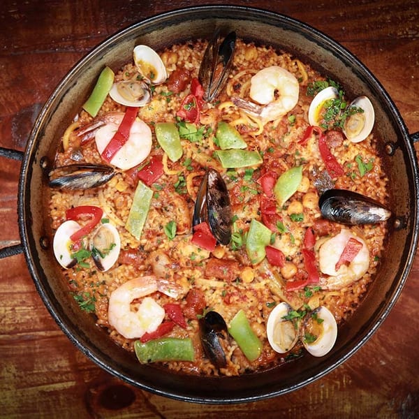 A large paella pan filled with seafood paella, featuring shrimp, mussels, clams, and vegetables.