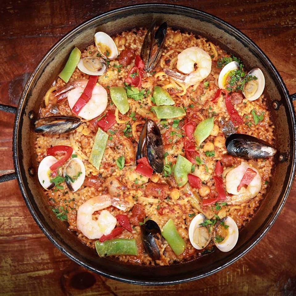 A large paella pan filled with seafood paella, featuring shrimp, mussels, clams, and vegetables.