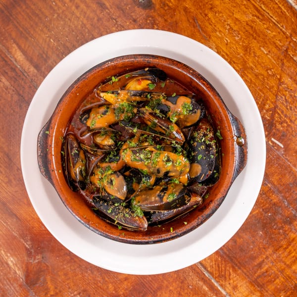 Steamed mussels in a rich sauce garnished with chopped herbs, served in a rustic dish on a wooden table.