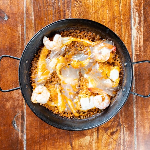 Overhead view of shrimp and melted cheese atop seasoned rice in a black skillet on a rustic wooden table.