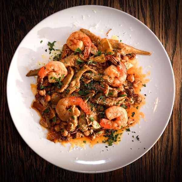 Shrimp and artichoke hearts with chickpeas and herbs in a rich sauce on a white plate.