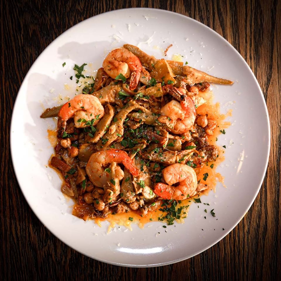 Shrimp and artichoke hearts with chickpeas and herbs in a rich sauce on a white plate.