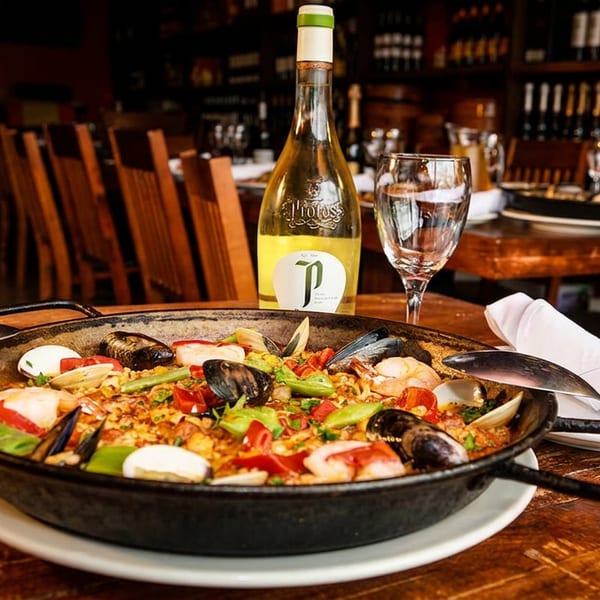A paella dish with seafood and vegetables, a bottle of white wine, and a wine glass on a wooden table.