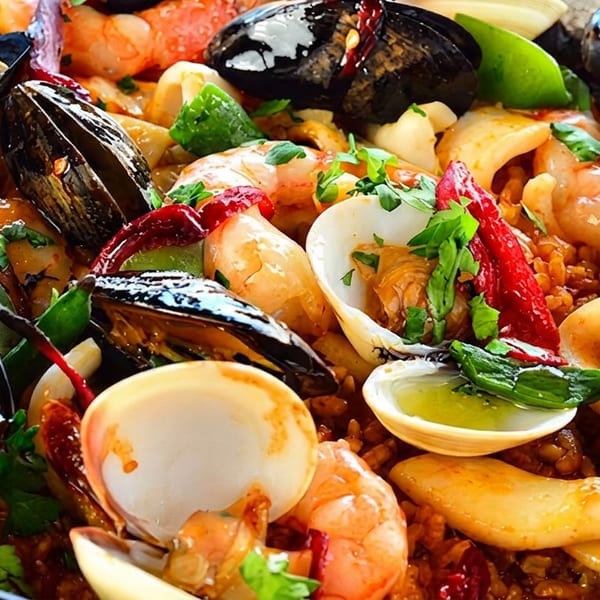 Close-up of a seafood paella with mussels, clams, shrimp, and squid in a black pan.