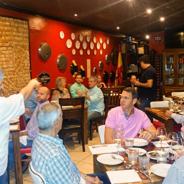 Diners seated at wooden tables in a restaurant with red walls adorned with decorative plates and pots.