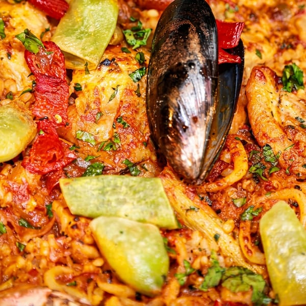 Close-up of a vibrant paella dish with mussels, shrimp, chicken, red peppers, and green beans.