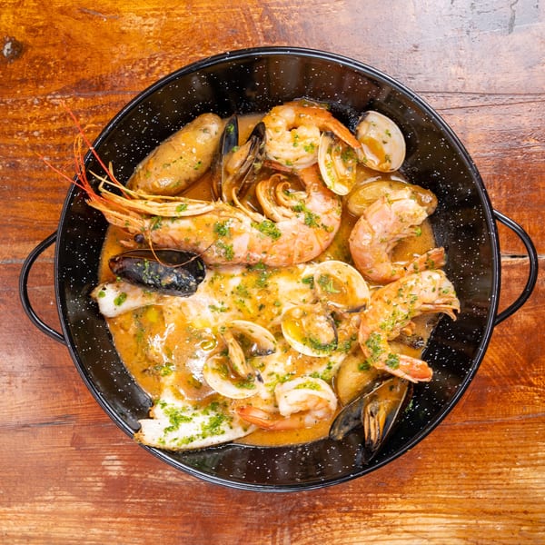 Overhead view of shrimp, mussels, clams, and fish in a herb-butter sauce served in a black pan on a wooden table.