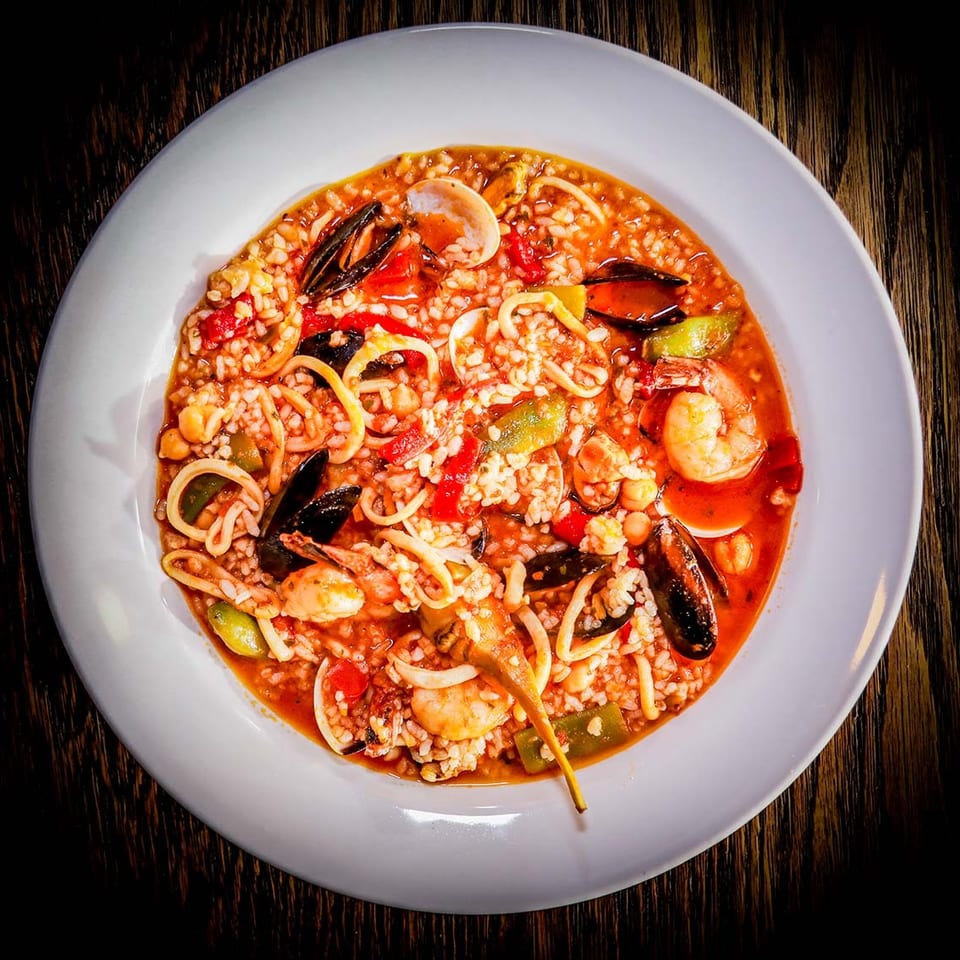 A white bowl filled with seafood paella, featuring shrimp, mussels, clams, and calamari.