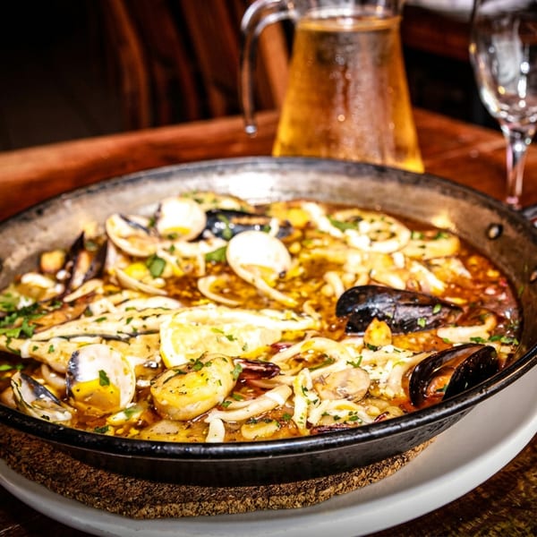 Seafood paella with mussels, clams, shrimp, and lemon in a pan on a wooden table.