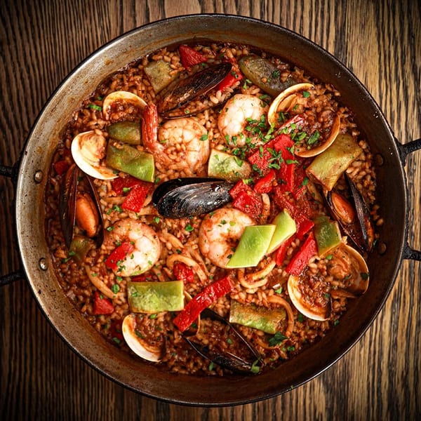 Close-up overhead view of a paella pan filled with seafood paella on a wooden table.