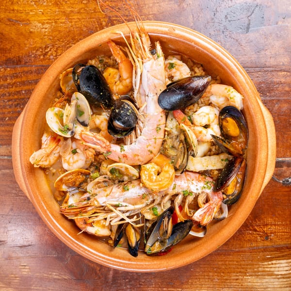 Overhead view of seafood paella with prawns, mussels, clams, and rice in a terracotta dish on a wooden table.