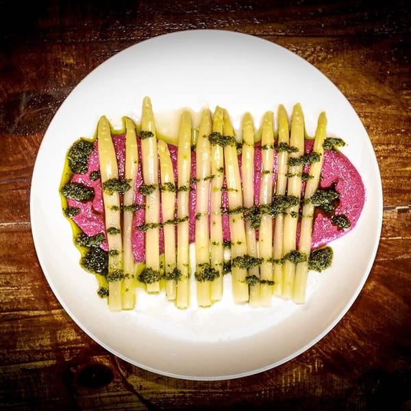 White asparagus spears with green pesto and a vibrant pink sauce on a white plate.