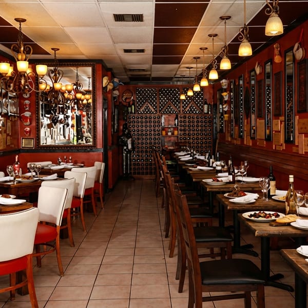 Cozy restaurant interior with red walls, chandeliers, set tables, and a large wine rack.