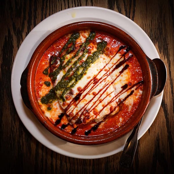 Baked pasta dish with melted cheese, red sauce, pesto, and balsamic glaze in a rustic bowl.