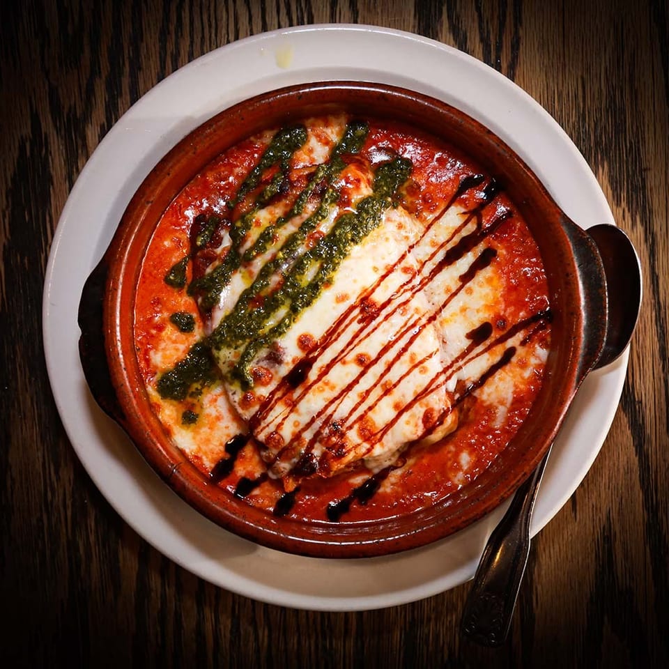 Baked pasta dish with melted cheese, red sauce, pesto, and balsamic glaze in a rustic bowl.