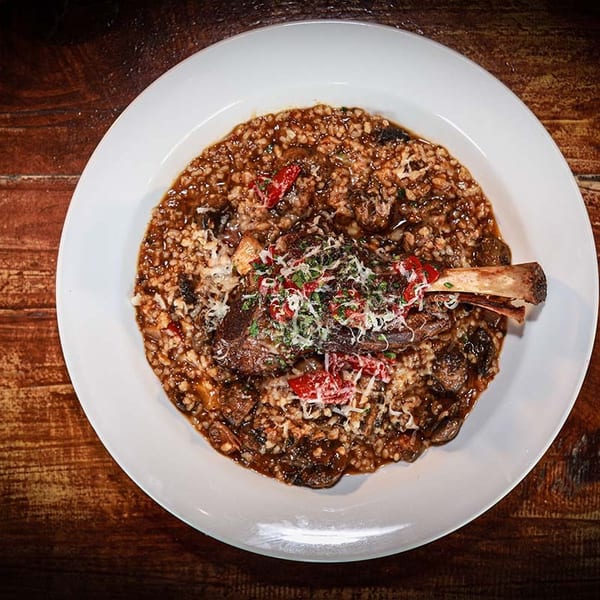 Braised lamb shank with risotto, garnished with cheese and herbs on a white plate.