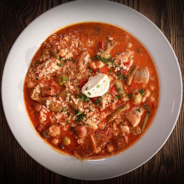 Hearty stew with chicken, rice, vegetables, and a dollop of sour cream in a white bowl.
