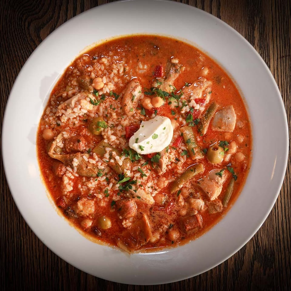 Hearty stew with chicken, rice, vegetables, and a dollop of sour cream in a white bowl.