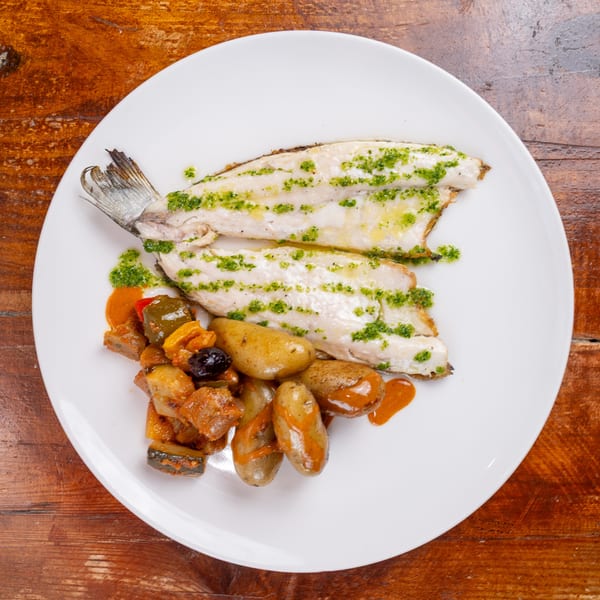 Grilled fish fillets topped with green herb sauce, served with roasted potatoes and vegetables on a white plate.